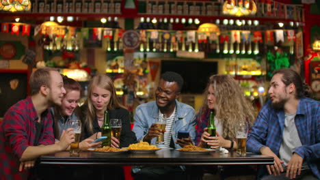 Eine-Gruppe-Junger-Männer-Und-Frauen-Sitzt-In-Einer-Bar-An-Einem-Tisch,-Trinkt-Bier,-Lachen-Und-Erzählt-Sich-Gegenseitig-Lustigen-Klatsch.